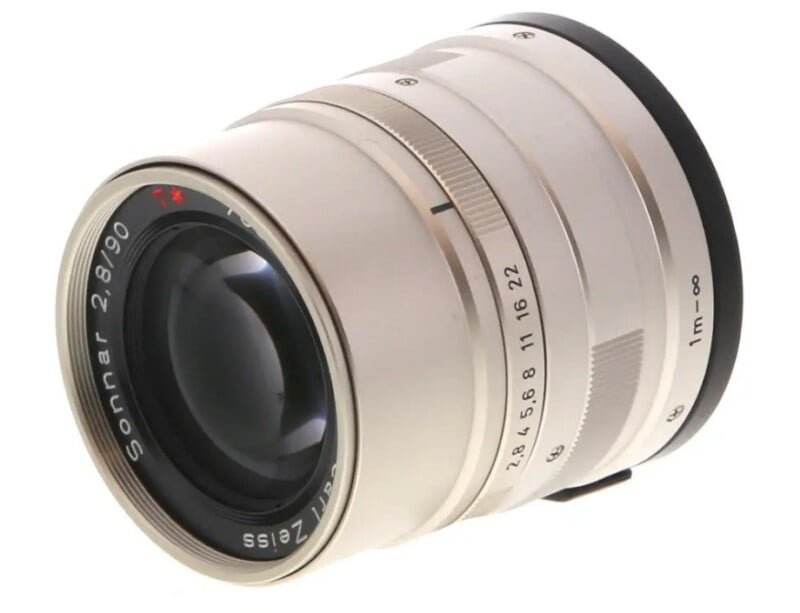 A silver camera lens with "Sonnar 2.8/90" and "Carl Zeiss" text engraved around the front element, featuring focus and aperture rings with marked settings.
